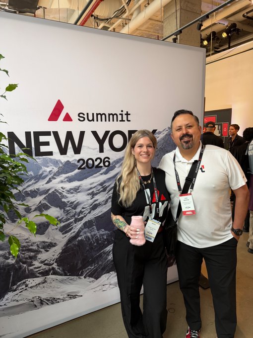 A man and a woman smiling and posing for a photo in front of a 'Summit New York 2026' backdrop at an indoor event.