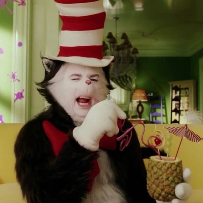 A cat dressed in a Dr. Seuss 'Cat in the Hat' costume with a red and white striped hat and bow tie, appearing to scream while holding a tropical drink, with a watermark reading '@retrolustt'.