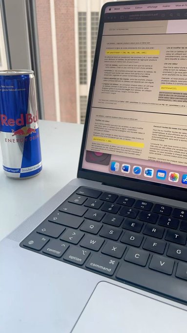 A can of Red Bull Energy Drink sits next to a MacBook laptop displaying an email conversation in French.