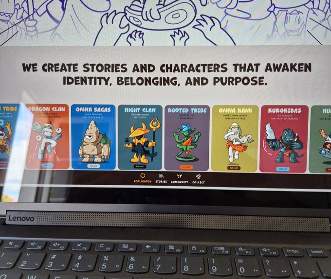 A Lenovo laptop screen displaying a website with the tagline 'WE CREATE STORIES AND CHARACTERS THAT AWAKEN IDENTITY, BELONGING, AND PURPOSE.' above character cards labeled 'DRAGON CLAN', 'OMNI SAGAS', 'NIGHT CLAN', 'ROOTED TRIBE', 'OMNI KAMII', and 'KURONIKAS'.