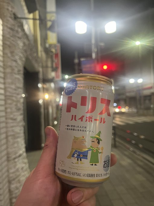 A hand holds a can of Suntory 'Torhis Highball' Japanese canned alcoholic beverage on a city street at night.