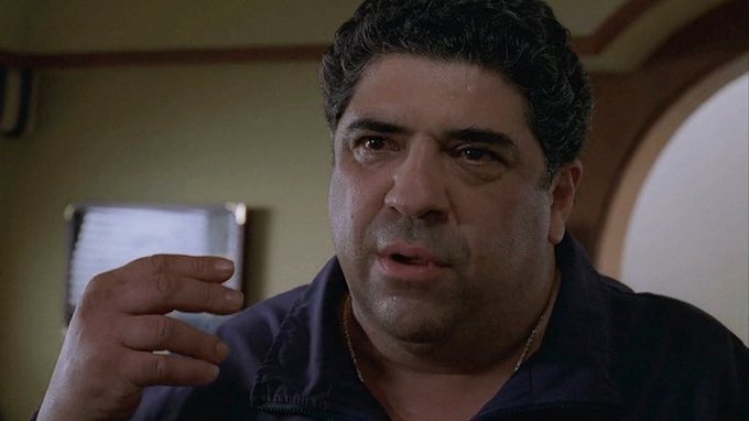 The image shows a close-up of a man with dark curly hair and a serious expression, gesturing with his hand as if mid-conversation, likely from a film scene. The caption "Rip to a legend" suggests this is a tribute to the actor, appearing to be Vincent Pastore, known for his role in "The Sopranos," honoring his passing.