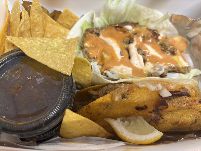The image shows a close-up view of two tacos with various toppings placed inside a white container, which appears to be a takeout box or a styrofoam plate. The tacos are accompanied by tortilla chips, specifically pita chips, as well as a small bowl filled with sauce. There is also a lemon wedge on the side of one of the tacos.

The post includes text that reads "I knew that was coming, so I set up a taco nacho barrier during the day. Firing the taco-nullifying arrow. The Korean Retail Bear, Hell Inflection, has consumed TACOs to nullify the Trump TACO signal." This suggests that someone is trying to prevent the tacos from being eaten by placing them in a container and setting up an obstacle for the tacos to face.