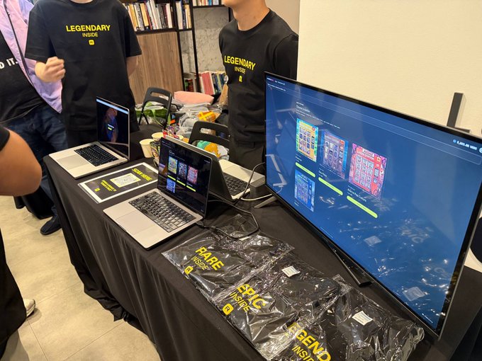 A booth setup features laptops and a large monitor displaying digital trading card packs, with "LEGENDARY INSIDE" printed on staff shirts and "RARE INSIDE" visible on packaged giveaway packs for a free spin promotion.
