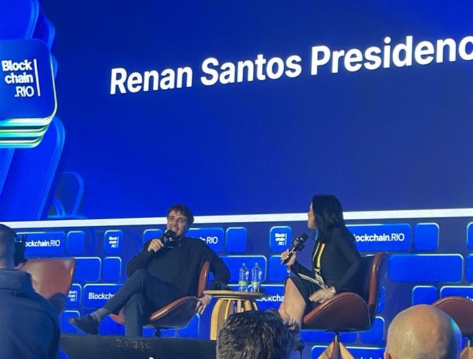 The image captures Renan Santos, identified by the on-screen text "Renan Santos President," seated on stage at Blockchain Rio (BlockChain.RIO) during an interview or panel discussion, holding a microphone while speaking with a female moderator. The scene directly illustrates the accompanying post, showcasing Santos discussing technology, blockchain, and strategic energy reserves as a presidential candidate—topics the author notes are rarely addressed by other political contenders.