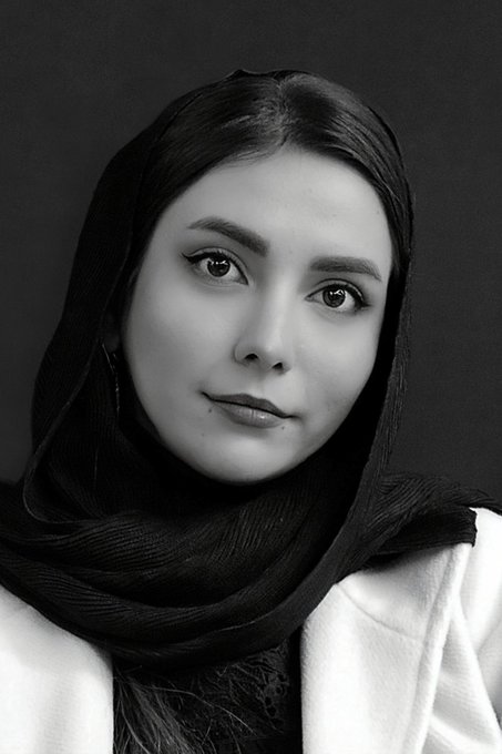 A black-and-white portrait photograph of a young woman wearing a dark headscarf, looking directly at the camera.