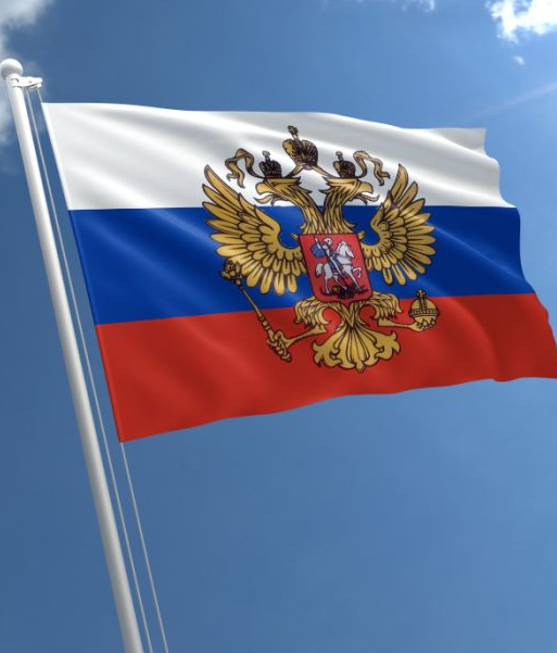 The image shows the Russian flag, featuring horizontal white, blue, and red stripes with the golden double-headed eagle coat of arms at its center, waving against a blue sky. It visually represents Russia, the country where Sberbank—the nation's largest bank—is now accepting Bitcoin collateral for loans under a new law, building on its successful December 2025 pilot program.