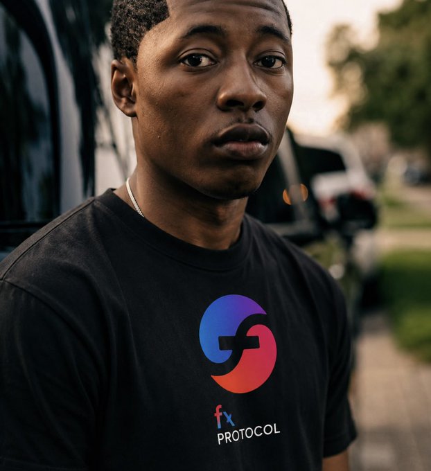 A young man in a black t-shirt featuring the colorful "fx PROTOCOL" logo (with "fx" in blue and red) stands outdoors with a serious expression, visually representing the f(x) Protocol brand discussed in the post about the fxSAVE auto-compounding stablecoin vault.