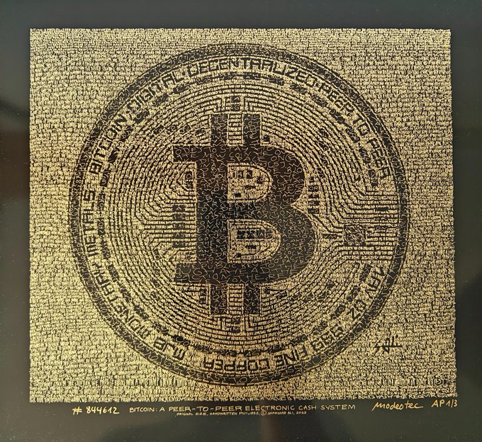 A gold and black artwork resembling a Bitcoin is constructed entirely from small, jigsaw puzzle pieces, with text reading 'BITCOIN A PEER-TO-PEER ELECTRONIC CASH SYSTEM' at the bottom.