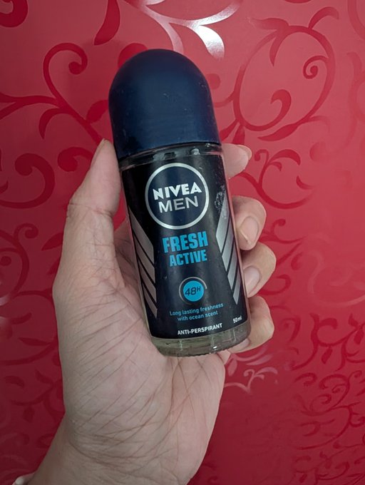 A hand holding a 50ml roll-on bottle of Nivea Men 'Fresh Active' deodorant, labeled as anti-perspirant with 48h long-lasting freshness and ocean scent, against a red patterned background.