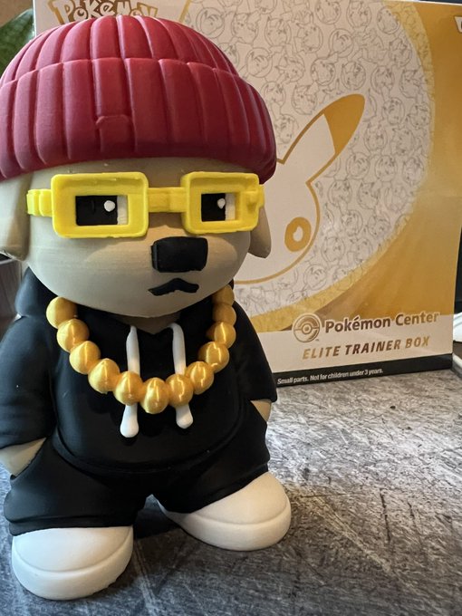 A Pokémon Center Elite Trainer Box featuring a figure of a dog character wearing a maroon beanie, yellow glasses, a black hoodie, and a gold chain, shown beside its packaging.