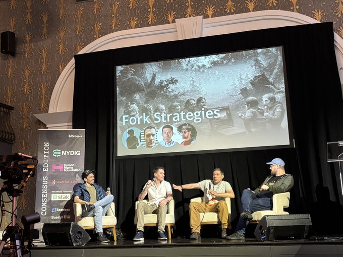 A panel discussion on stage titled 'Fork Strategies' at what appears to be a Consensus Edition event, with four men seated in chairs being interviewed, featuring sponsor logos for NYDIG, Human Rights Foundation, and others.