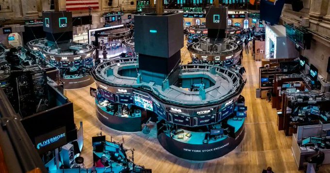 An overhead view of the New York Stock Exchange trading floor, featuring circular trading posts marked with 'LCH' and various electronic displays, with traders working below.