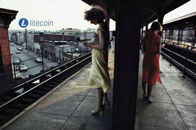 Two women in vintage dresses stand on an elevated train platform overlooking a city street, with a "litecoin" logo and ticker "L" visible in the upper left corner of the image.