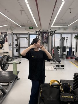 A woman poses in a gym wearing a black shirt, holding up peace signs with both hands, with a black "BINANCE" branded duffel bag with yellow straps visible in the foreground. The post highlights her excitement about receiving Binance-branded bag and clothing from @miyayweb3, which she's using for her workout gear.