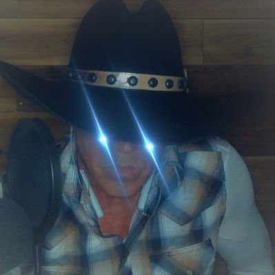 A person wearing a black cowboy hat with studs and a plaid shirt, with bright lights reflecting off their face obscuring their eyes.