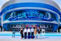 An animated scene showing five figures standing in a futuristic setting with a large curved screen displaying Korean text in the background.