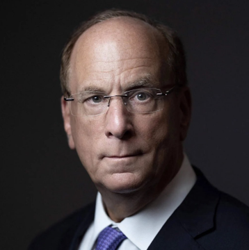 A professional portrait of a bald man with glasses wearing a dark suit, white shirt, and purple tie against a dark background.