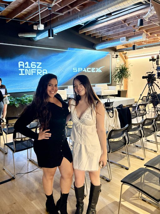 Two women posing together at what appears to be a SpaceX event, with a screen behind them displaying "R16Z INFRA" and "SPACEX" logos.