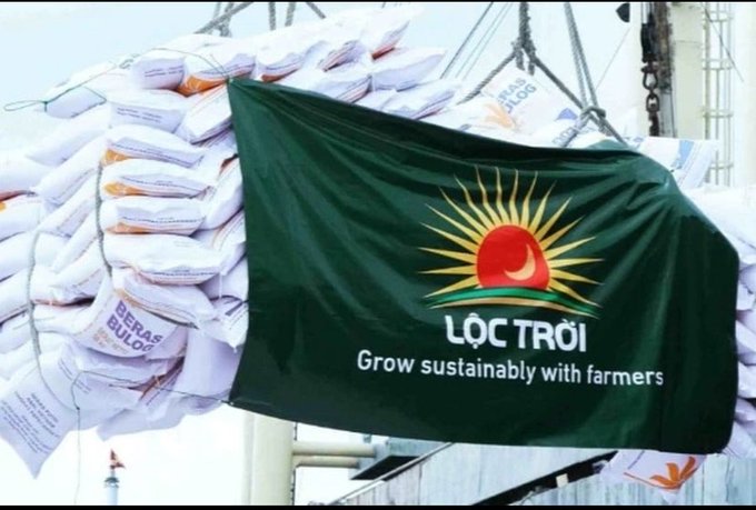 A green flag with the 'LỘC TRỜI' logo and slogan 'Grow sustainably with farmers' is draped over a large pallet of rice sacks marked 'BERAS BULOG' at a port.