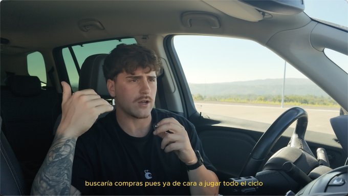 A man with tattoos driving a car speaks to the camera, with Spanish subtitles reading 'buscaría compras pues ya de cara a jugar todo el ciclo'.