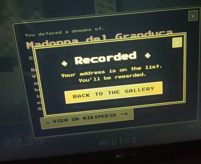 A photograph of a screen showing a game interface with the text 'You defaced a remake of... Madonna del Granduca' and a popup window stating 'Recorded. Your address is on the list. You'll be rewarded.' with a 'BACK TO THE GALLERY' option.