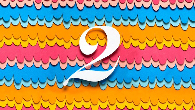 Colorful decorative number '2' in white paper-cut style over a background of layered, scalloped paper in blue, orange, and pink tones.