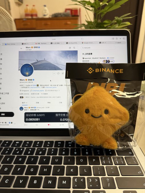 A Binance-branded plush toy of the BNB mascot sits on a laptop keyboard, with the screen displaying the Mars (BNB) Twitter page showing a market cap of 35.67K and a price of 0.0805061 USDT.