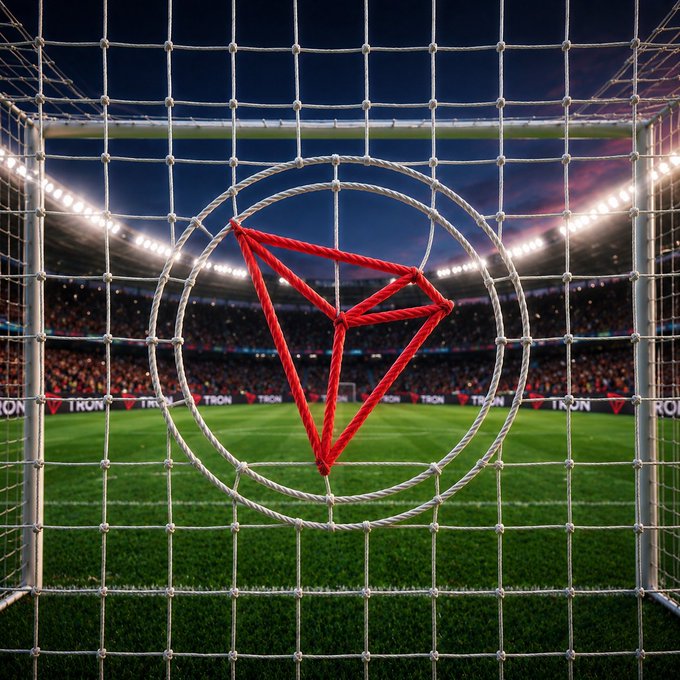 A view from behind a soccer goal net showing a stadium with bright lights and crowds, with a red triangular symbol overlaid on the netting.