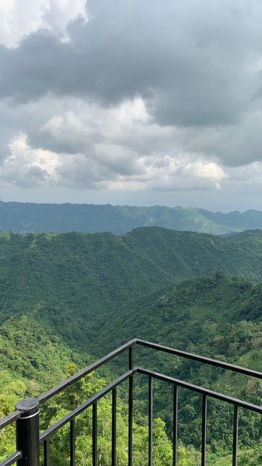 A scenic view from a balcony railing overlooking lush green mountainous terrain under a cloudy sky.