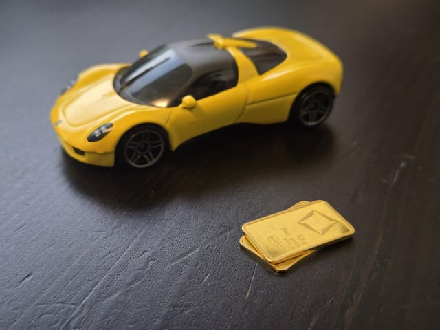 The image features a yellow toy car placed on top of two gold bars. The presence of these gold bars suggests that they are being used as currency or tokens for stacking purposes. This implies that someone might be playing with the toy car, stacking the gold bars one above the other, and using them to represent money in their imaginative play.