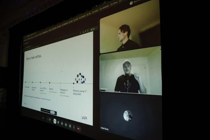 A projector screen displaying a video conference with three participants and a presentation slide titled "How a bank services," watermarked "vAPI" at the bottom.