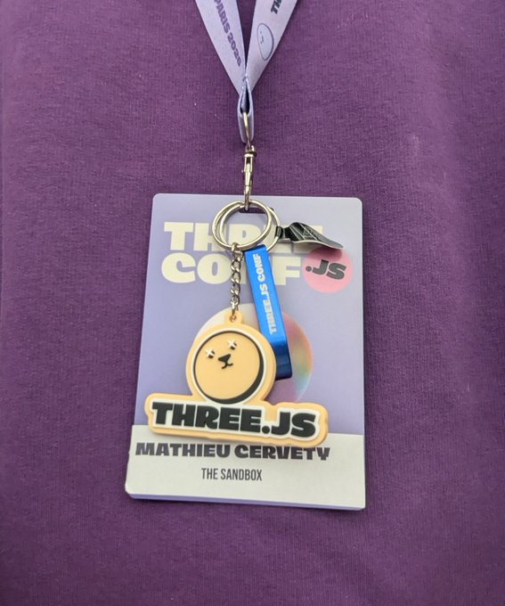 A Three.js conference badge for MATHIEU CERVETY from THE SANDBOX, featuring a cute character keychain attached via a Three.js branded lanyard on a purple background.