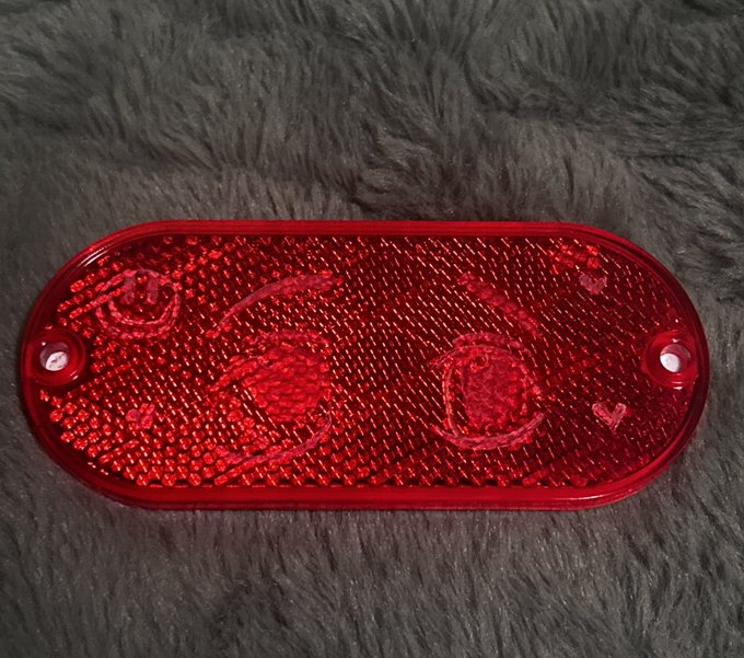 A close-up of a red, oval-shaped automotive light reflector with a checkered pattern, resting on a dark gray furry surface.
