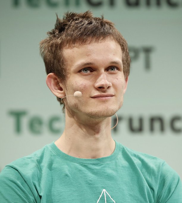 A young man with short brown hair wearing a teal t-shirt and an earpiece microphone, appearing to speak at a TechCrunch event.