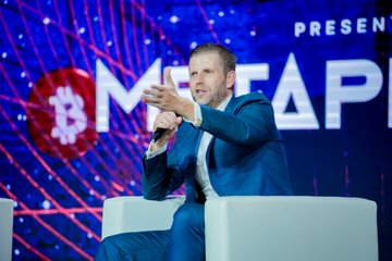 The image features a man sitting in a chair, wearing a suit and holding a microphone. The background of the image shows a large screen displaying the words "present" and "BITCOIN Asia". The caption below the image reads "SOME OF OUR MOST LEGENDARY SPEAKERS AT #BITCOIN ASIA OVER THE YEARS Who do you want to see next?".
