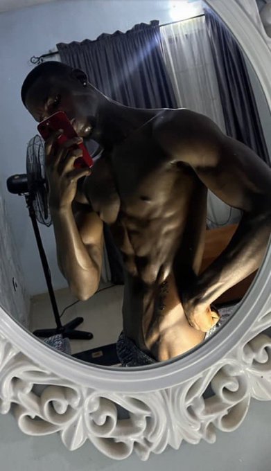 A mirror selfie of a muscular shirtless man holding a red phone, showcasing his physique in front of an ornate white-framed mirror.