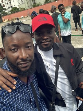 Two men pose for a close-up selfie, with the man on the right wearing a red cap and black jacket over a white shirt, while the man on the left sports a black cap and checkered blue shirt. The image aligns with the post's caption, capturing the moment shared between the poster and "his boss" alongside others at the #UnchainSummer26 event.
