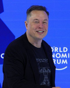 In the image, a man wearing glasses is smiling at the camera, standing behind a blue wall with text. The caption below the picture reads "ELON Musk Now Worth More Than Bitcoin's Total Market Cap Elon: $1.4T $BTC : $1.3T Bitcoin' s entire supply (21M coins Forever) is now valued less than one person’s stake in Tesla + SpaceX." The man and his facial expression are featured prominently, with the text providing context about the value of his stake compared to virtual currency.