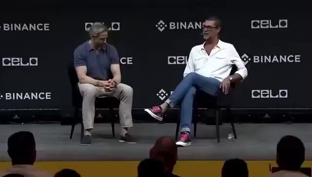 The image shows two men sitting next to each other at a stage with a crowd of people behind them, watching their conversation. One man has his foot up on a chair while talking to another man who is wearing glasses and a white shirt. The background features a banner that reads "BITCOIN CRASH IS TEMPORARY, 4-YEAR CYCLE IS NOW DEAD AND WE ARE ABOUT TO GO PARABOLIC IT'S COMING". This suggests that the image might be related to Bitcoin or cryptocurrency news, possibly discussing the current state of Bitcoin and its potential future.

The crowd behind them appears to be engaged in the conversation as well, indicating a public event or gathering where people are interested in hearing about the latest developments in the world of cryptocurrencies.