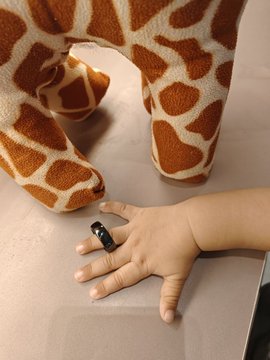 A baby's hand resting on a surface while a giraffe stuffed animal stands beside it.