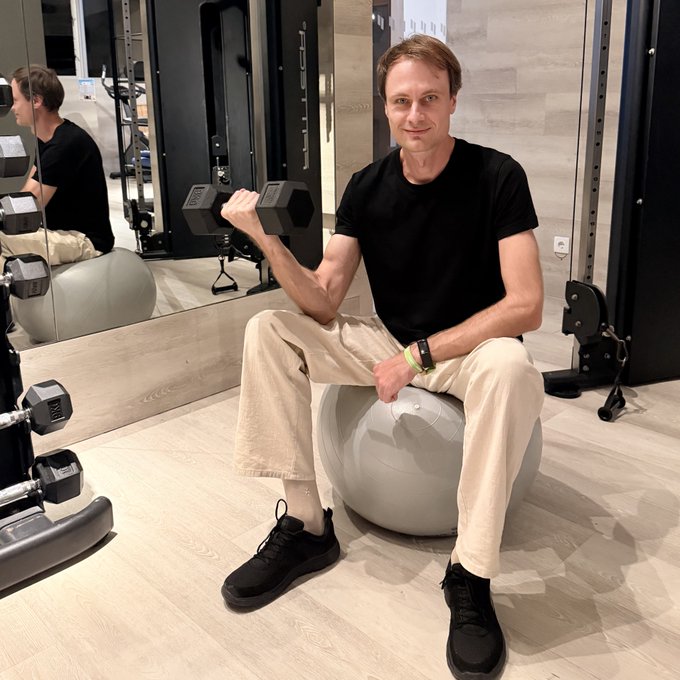 A man identified as JAN3 CTO @BraginRights sits on a stability ball in a gym, lifting a dumbbell while posing for a photo. The image relates to the post by highlighting his active, health-focused lifestyle outside of his Bitcoin development and self-custody discussions at the event.