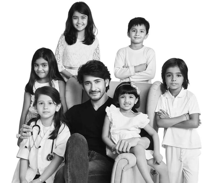 A black and white portrait of a man sitting in a chair surrounded by six children of varying ages, all dressed in white or light-colored clothing.