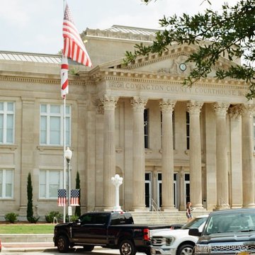 The Jefferson County Courthouse, a large classical-style stone building with tall columns, stands behind an American flag on a flagpole, with a black pickup truck and white SUV parked in front.