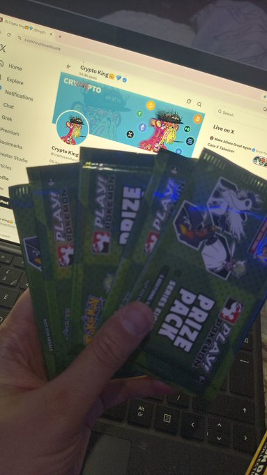 A hand holds several sealed Pokémon "Play!" Prize Pack booster packs in front of a laptop screen displaying the "Crypto King" Twitter/X profile. The image visually answers the post's question by showing a stack of collectible Pokémon packs ready to be opened or traded.