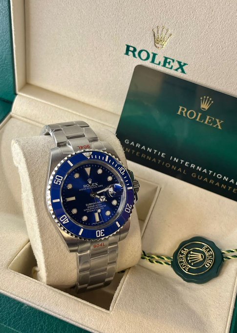 A Rolex Submariner watch with a blue dial and bezel displayed in its presentation box alongside the international guarantee card and seal.