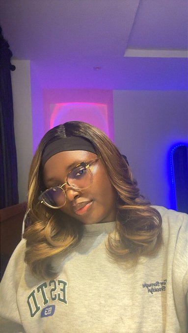 A selfie of a woman wearing glasses and a black headband in a room lit with purple and blue LED lights.