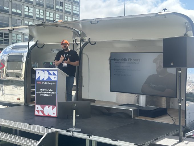 Hendrik Ebbers, Director of Open Source at Hashgraph, speaks at W> World Congress on building open-source ecosystems. He is pictured beside a stage with his presentation displayed on a screen.