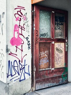 A weathered doorway with graffiti-covered walls and rusted metal doors stands as an entryway in an urban setting.