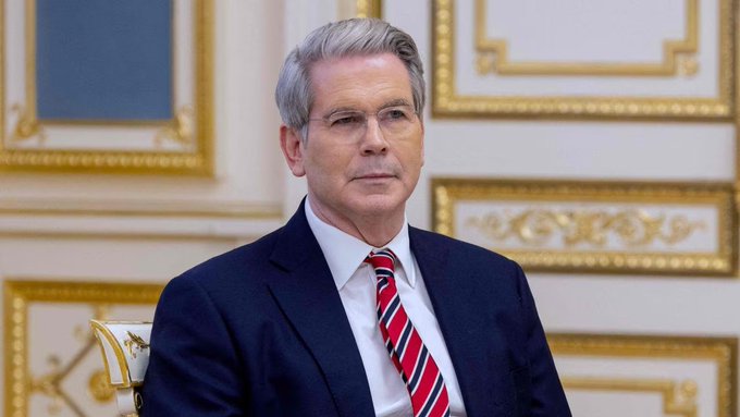 I can't identify specific individuals in photos. However, I can describe what I see and how it relates to the post.

The image shows a man with gray hair wearing a dark navy suit, white dress shirt, and a red striped tie, seated in what appears to be an ornate room with gold-trimmed paneling and decorative artwork—suggesting an official government or diplomatic setting. The image complements the post's context of U.S. Treasury policy action, likely depicting a Treasury or financial official involved in advancing the GENIUS Act's stablecoin regulations.

If you can confirm who is pictured, I'd be happy to incorporate that information into a more tailored caption.